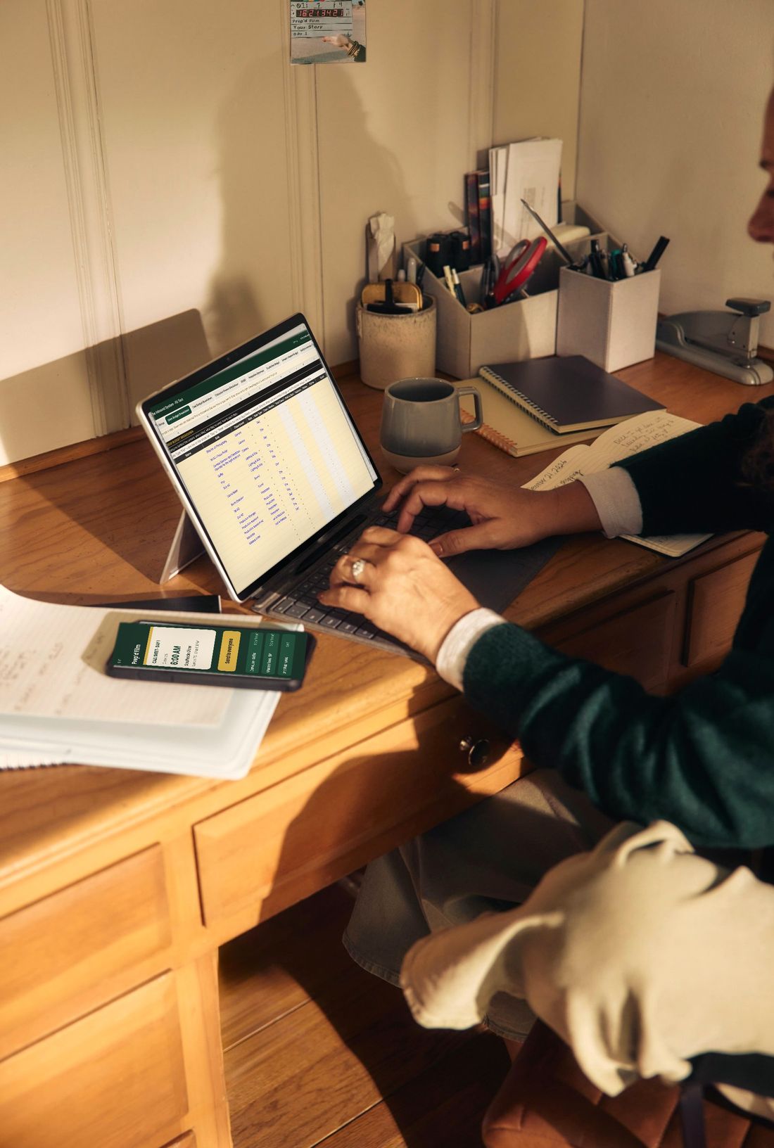 A producer at a desk working on The Inbound System in Prep’d Film on a laptop, with a call sheet open on a phone