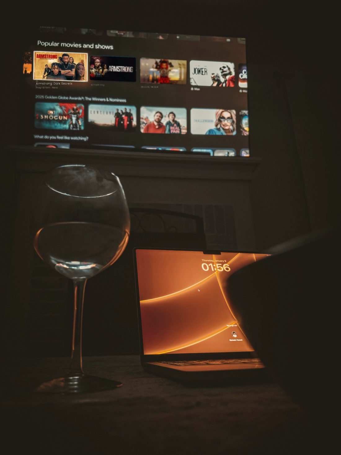 A living room at night: three indie films on the TV, a laptop glowing on the table beside a wine glass