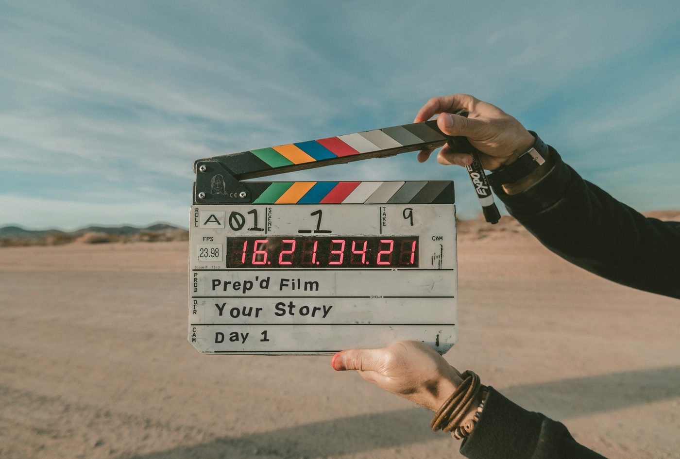 A film slate reading Prep’d Film, Your Story, Day 1, held up on location